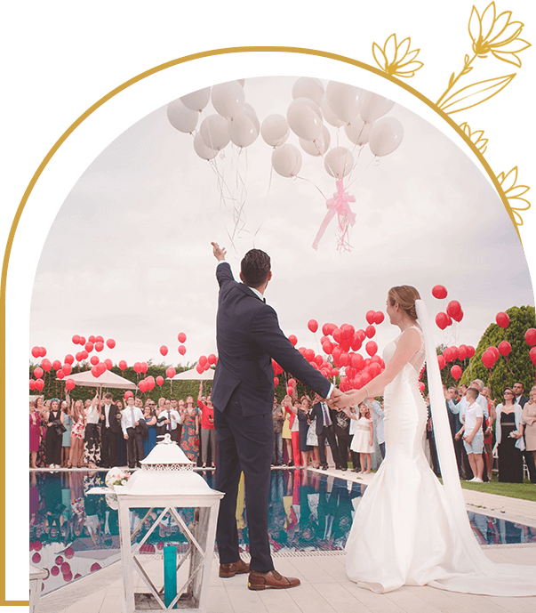 A couple is holding balloons while standing in front of an arch.