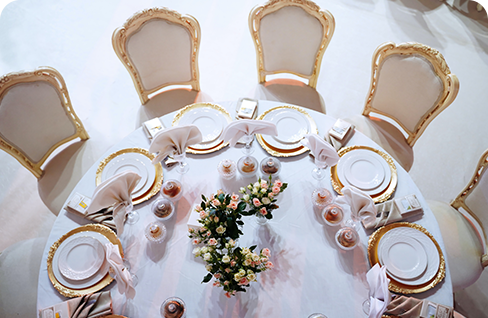 A round table with white and gold plates, napkins, and flowers.