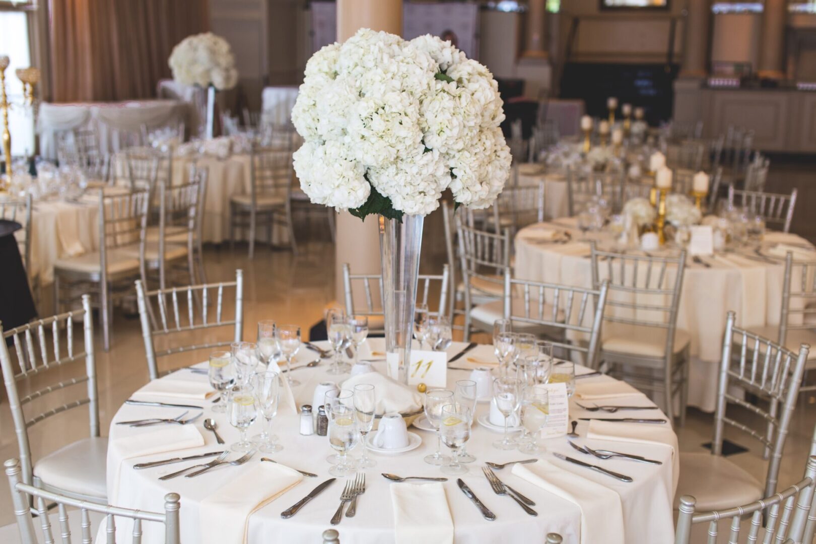 A table with white linens and silver chairs.